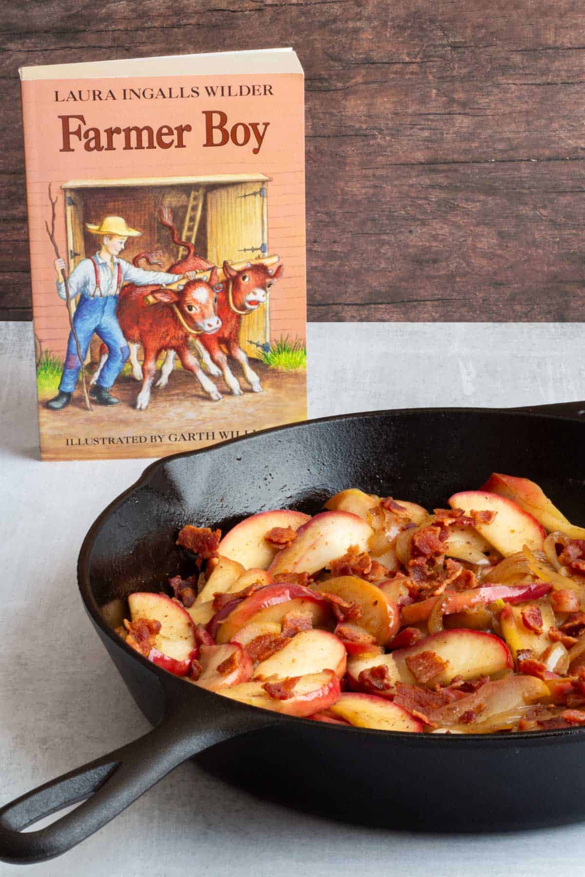 The book "Farmer Boy" next to a cast iron skilet of cooked Apples and Onions.