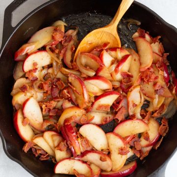 Fried Apples and Onions in a cast iron skillet with a wooden spoon.