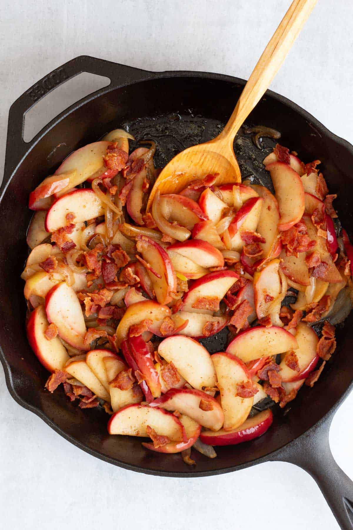 Fried Apples and Onions in a cast iron skillet with a wooden spoon.