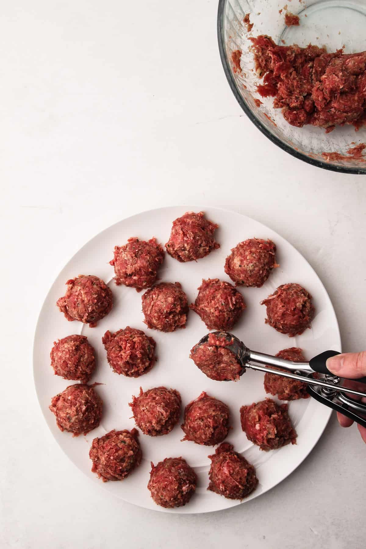 A hand using a scoop to portion meatballs onto a plate.