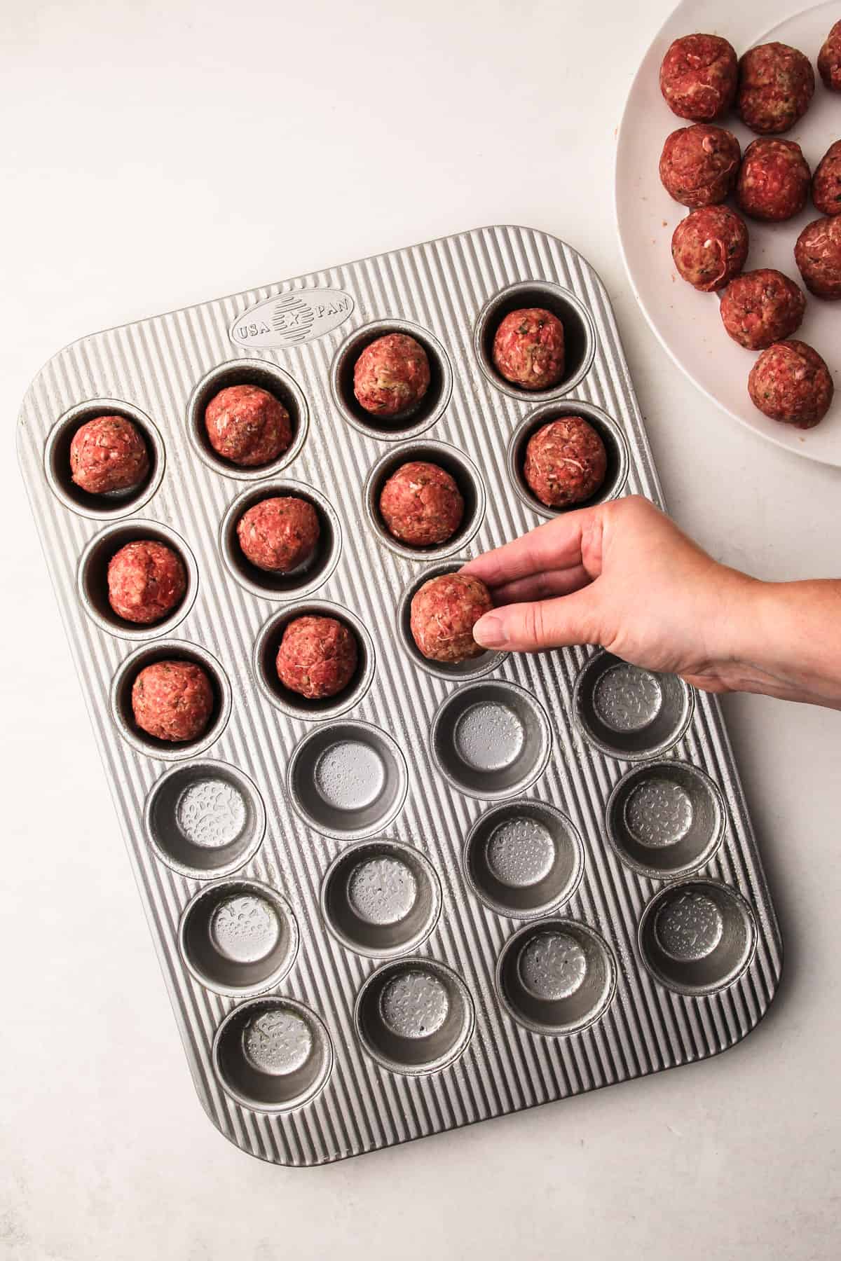 A hand placing a rolled meatball into a mini muffin tin for oven-baked meatballs.