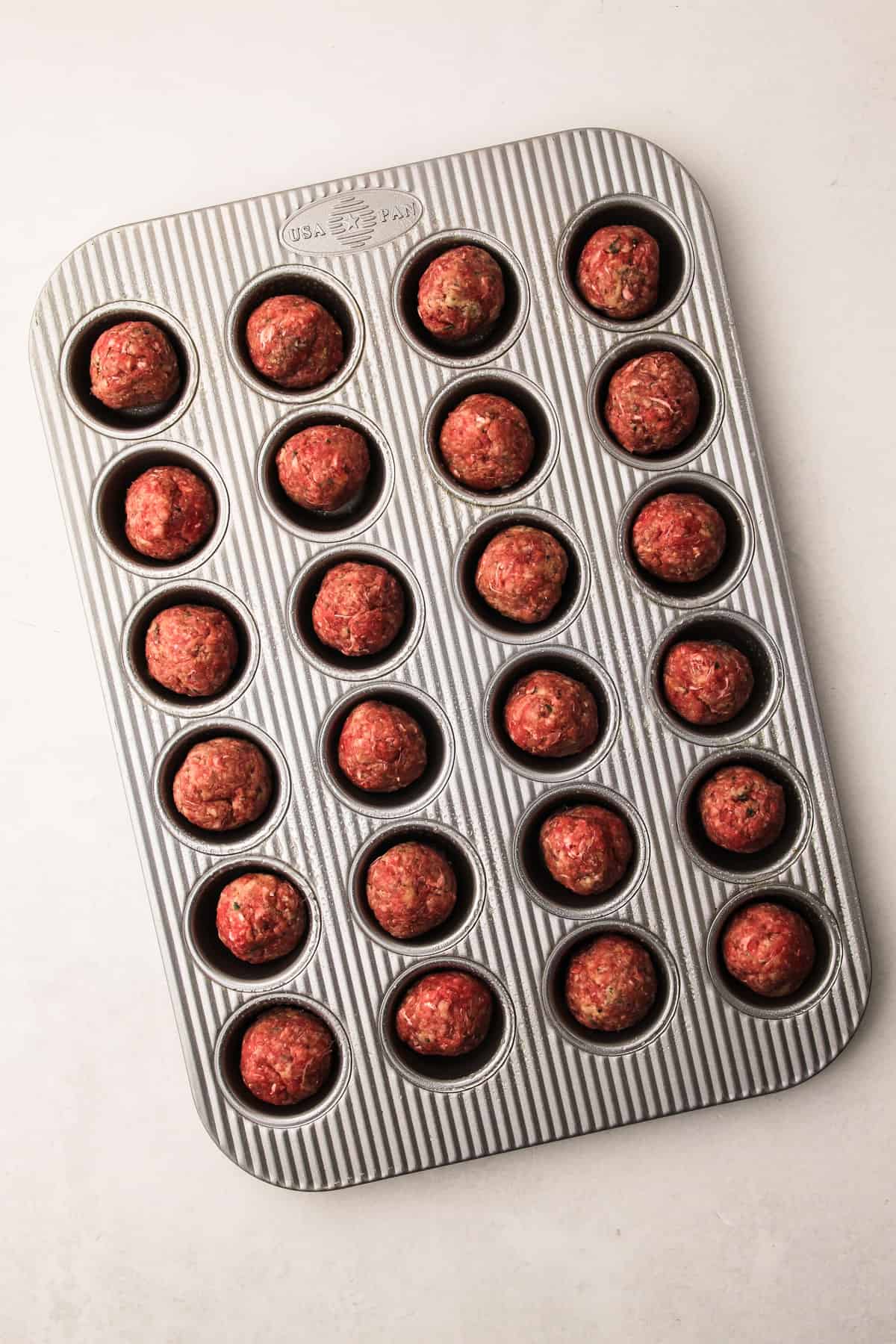 Shaped oven-baked meatballs in a mini muffin tin, ready to bake.