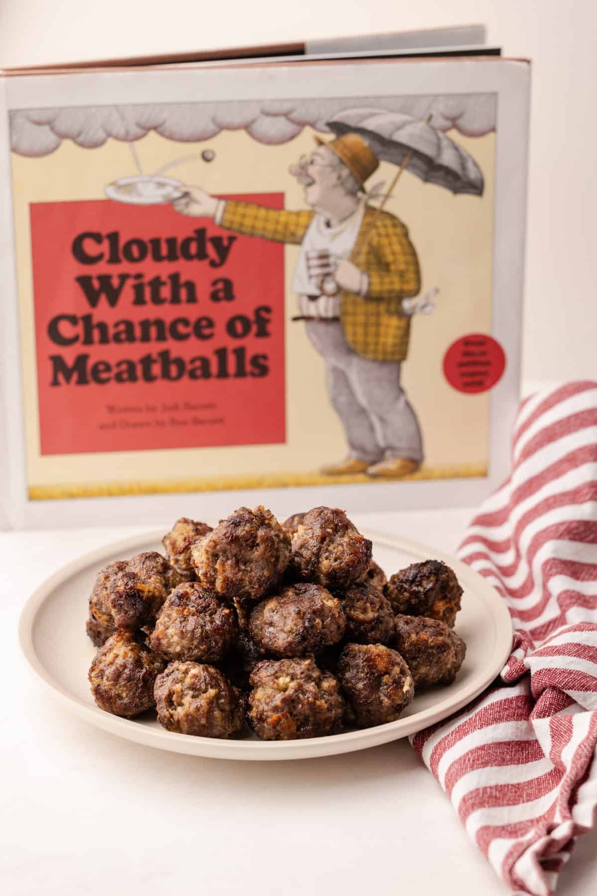 A pile of oven-baked meatballs on a plate, with the book "Cloudy with a Chance of Meatballs" in the background.