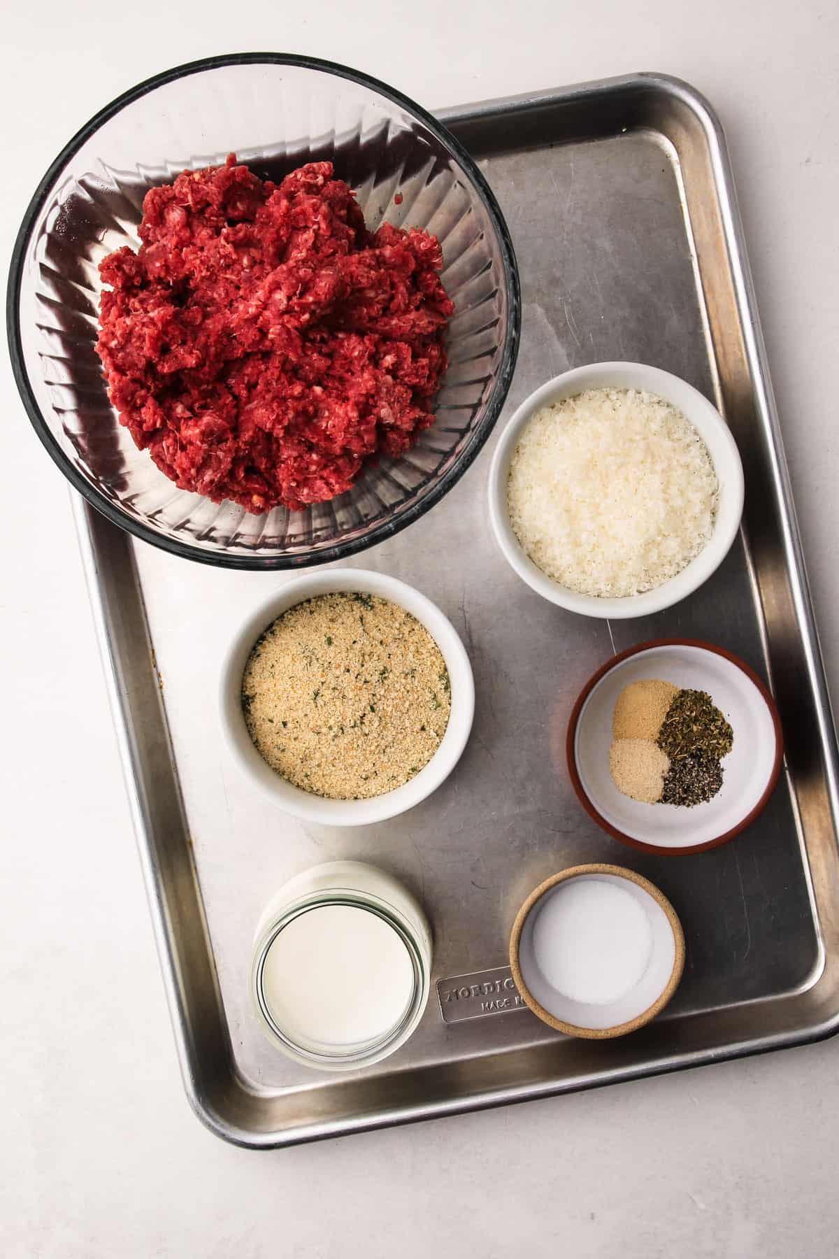 The ingredients for oven-baked meatballs measured into bowls on a baking sheet.