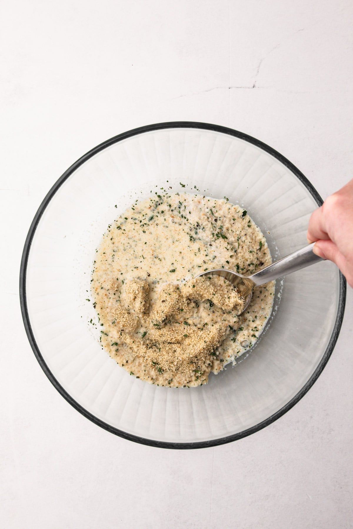 A hand using a spoon to stir together breadcrumbs and milk for oven-baked meatballs.