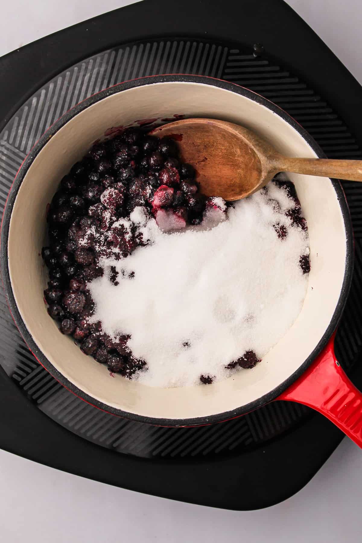 A wooden spoon stirring together the ingredients for wild Maine blueberry jam in a saucepan.