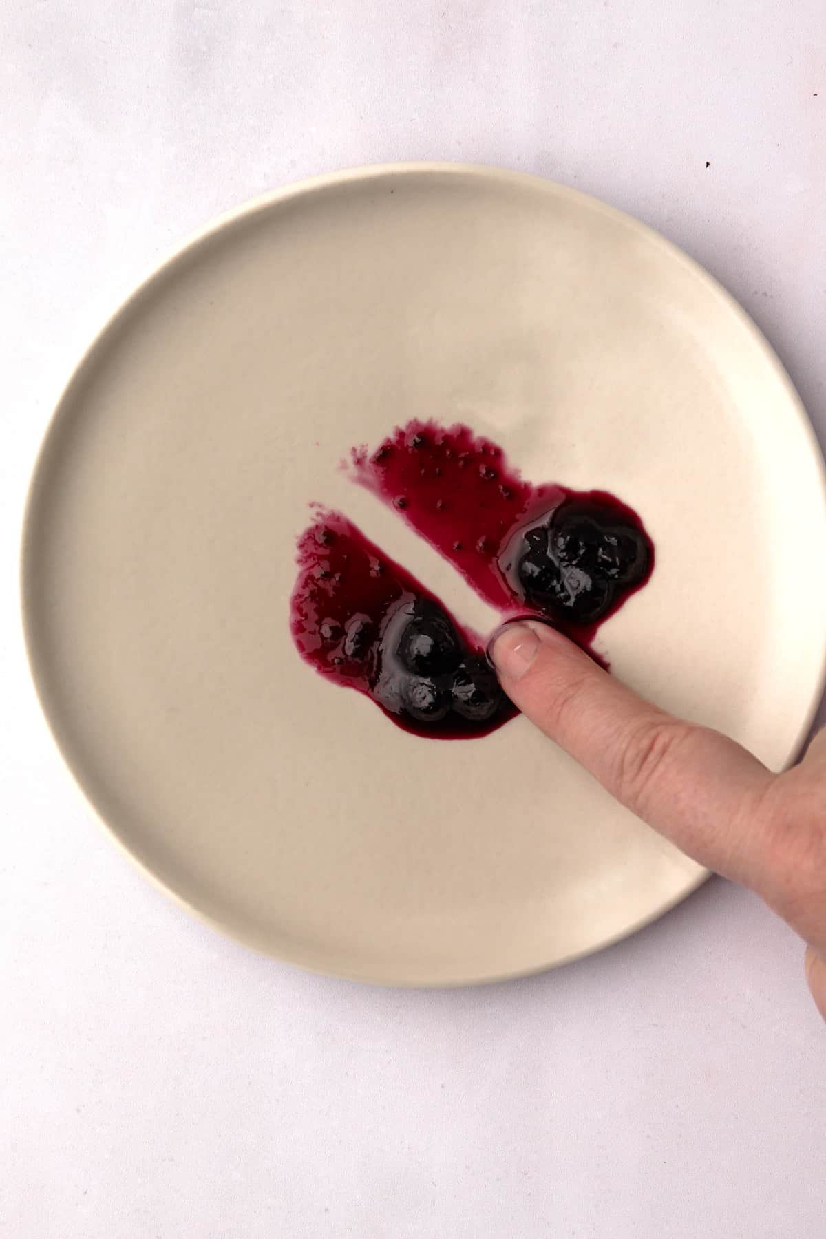 A finger dragging a clear trail through a dollop of cooked wild Maine blueberry jam on a plate.