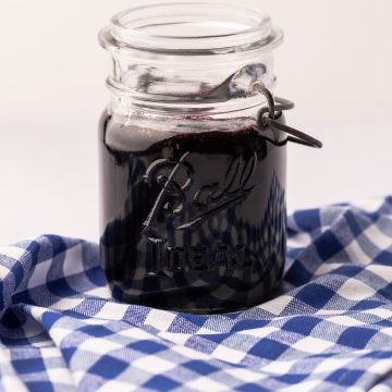 A jar of wild Maine blueberry jam on a blue and white gingham cloth.