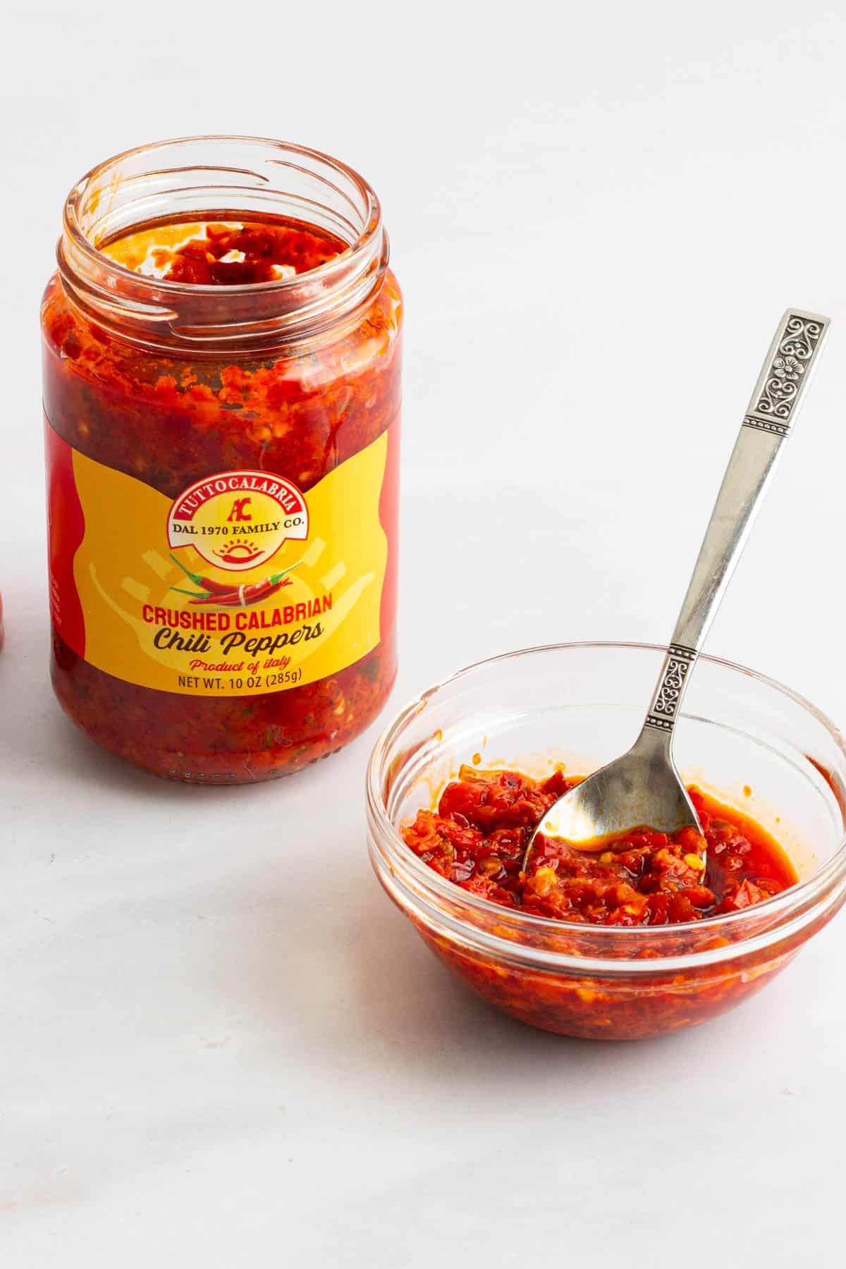 A jar of and a bowl with a spoon in it of crushed Calabrian chiles for Spaghetti with Garlic and Oil.