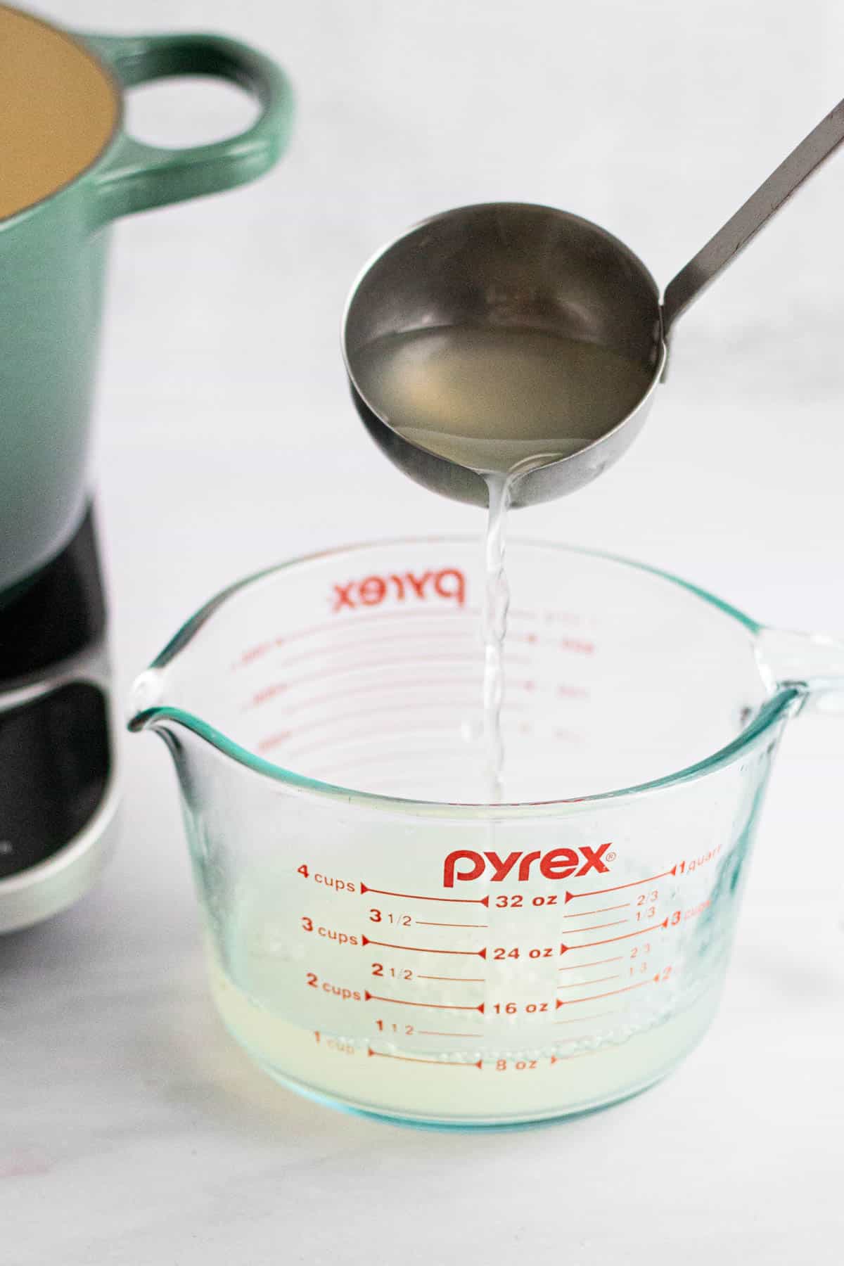 A ladle pouring pasta water into a measuring cup for Spaghetti with Garlic and Oil.