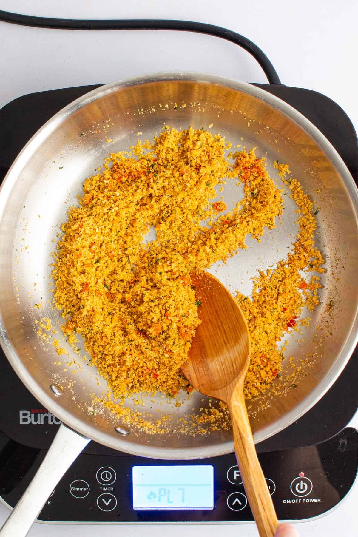 A wooden spoon stirring spicy Calabrian breadcrumbs in a skillet for Spaghetti with Garlic and Oil.