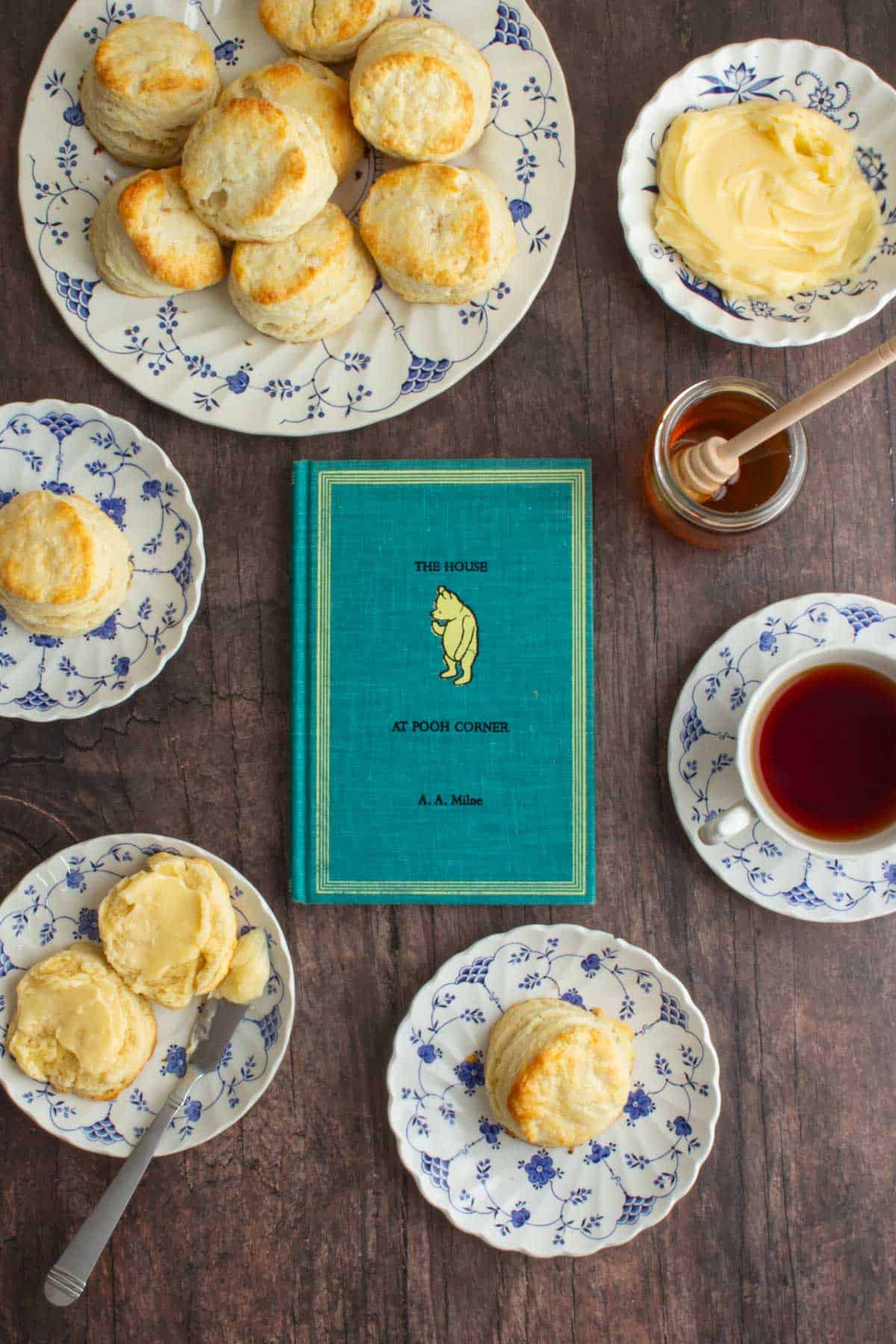 The cover of the book The House at Pooh Corner next to plates of cream scones with homemade honey butter.