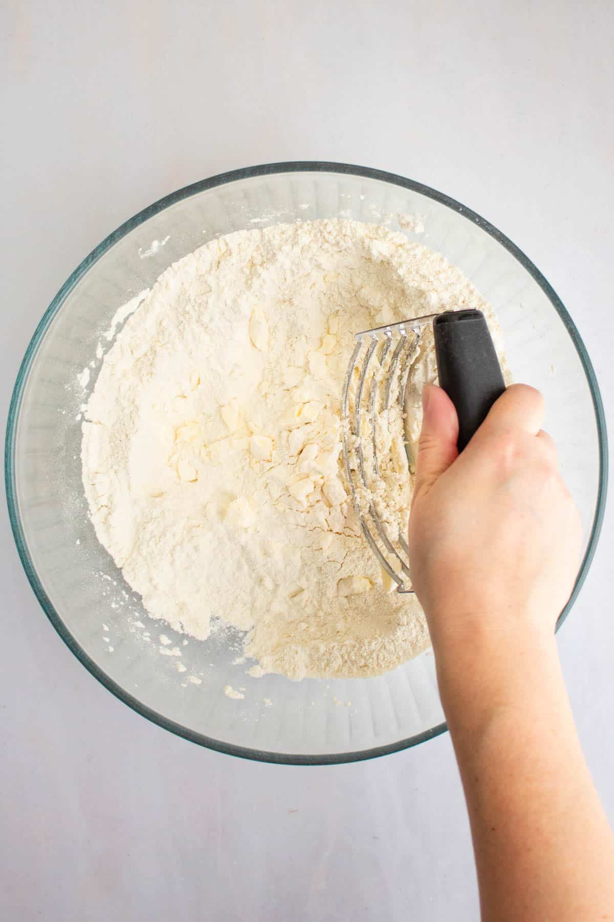 A hand using a pastry blender to cut butter into flour for an easy scones recipe.