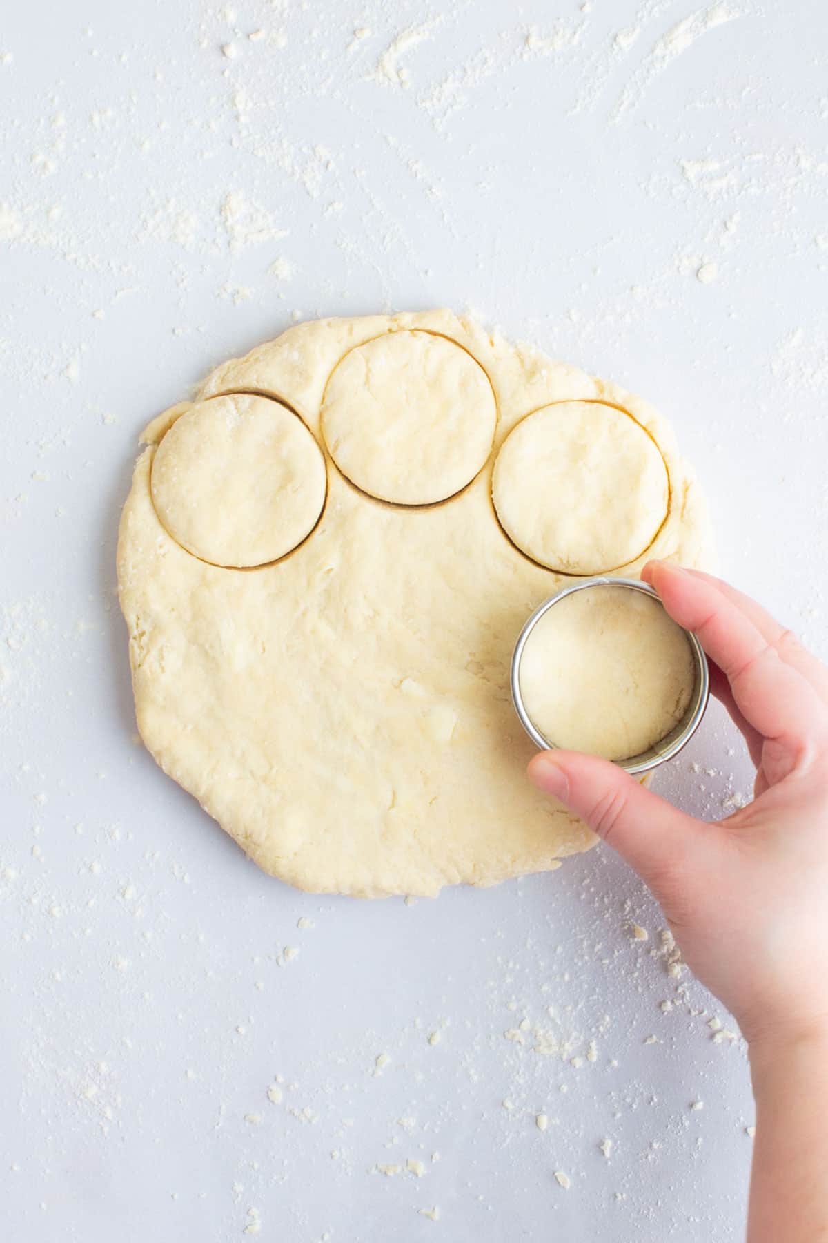 A hand using a round cookie cutter to cut out circles of dough for an easy scones recipe.