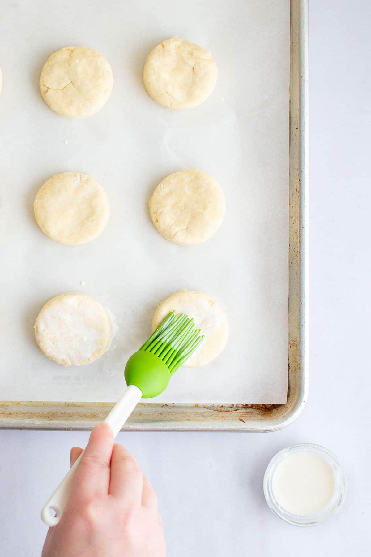 A hand using a pastry brush to brush cream on top of dough rounds for an easy scones recipe.