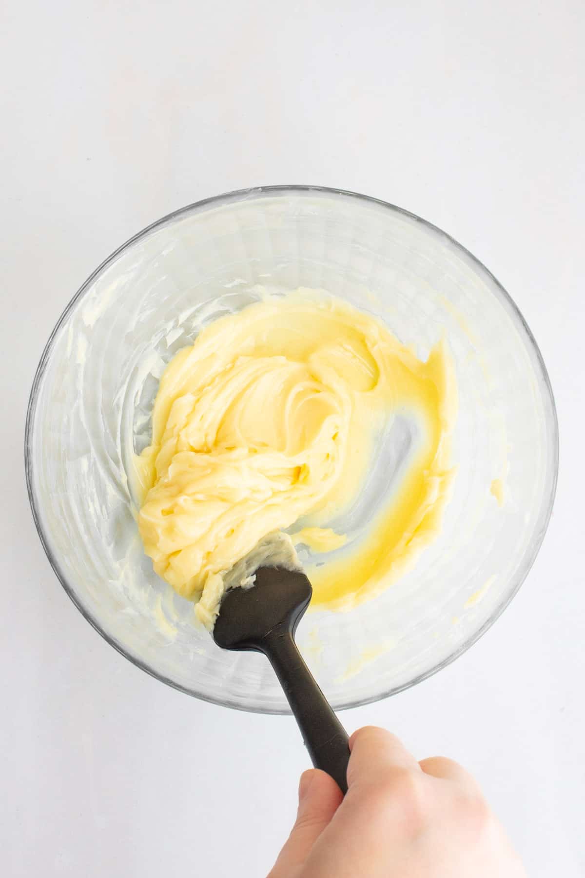 A hand using a rubber spatula to stir together homemade honey butter.