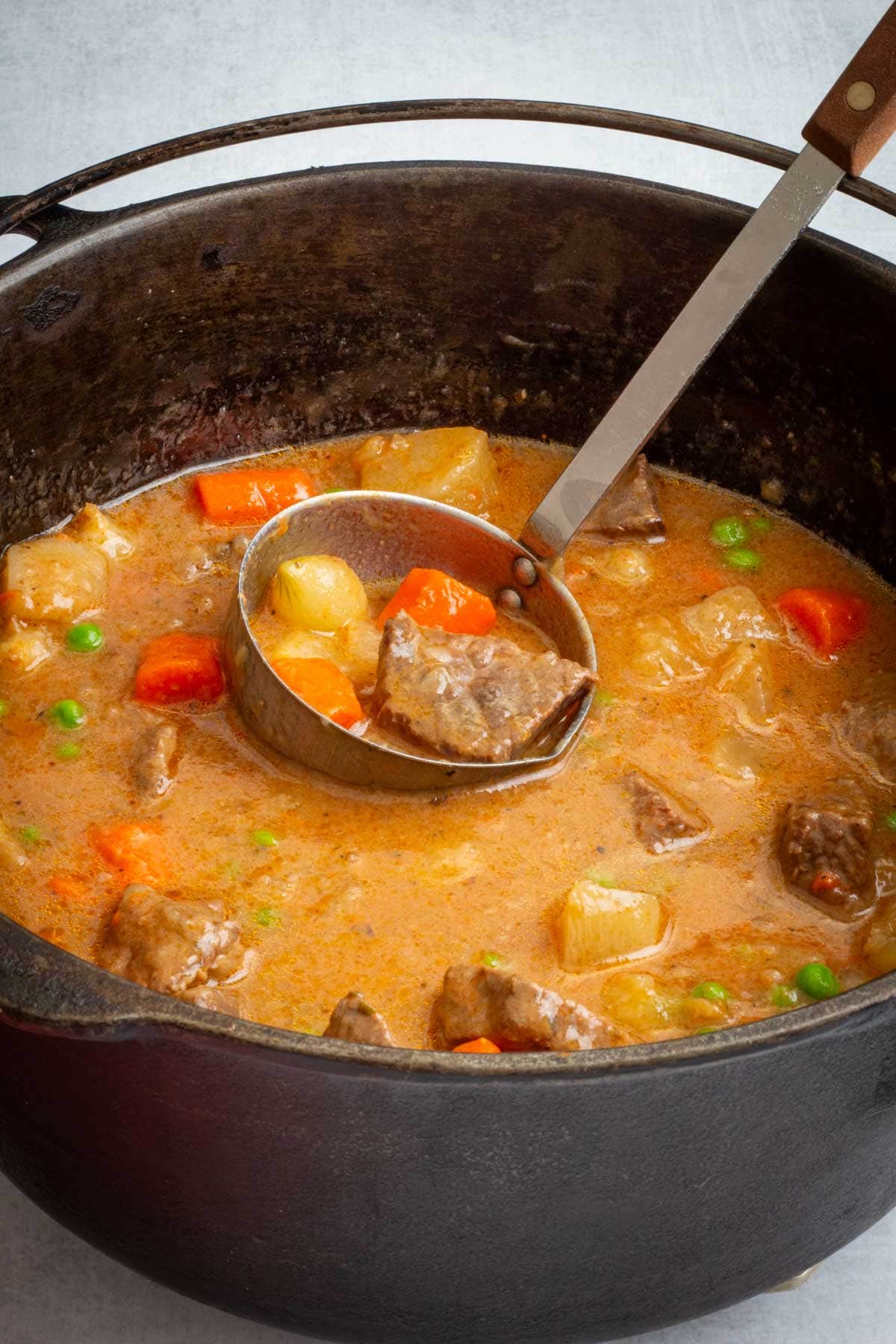 A pot and ladle filled with Dutch Oven Beef Stew.