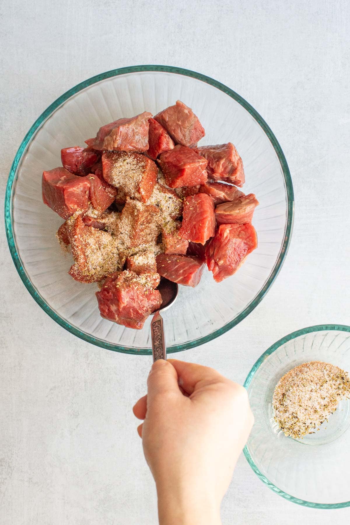 A hand stirring seasonings into cubed beef for Dutch Oven Beef Stew.