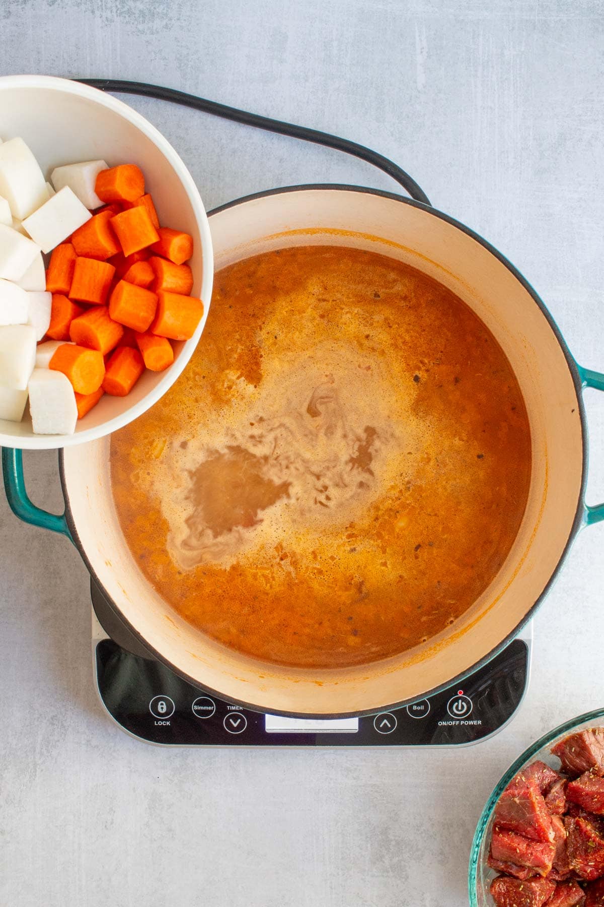 Chopped carrots and turnips about to be poured into broth in a pot for Dutch Oven Beef Stew.