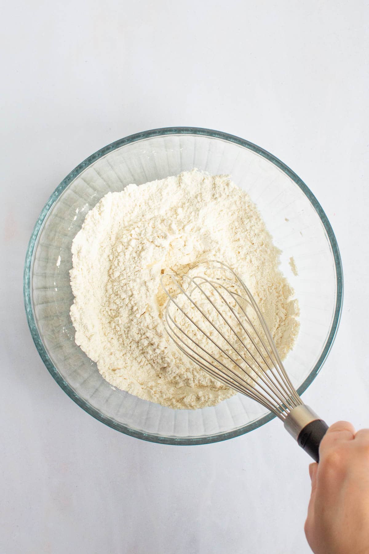 A hand using a whisk to whisk together dry ingredients for small-batch chocolate chip cookies in a bowl.