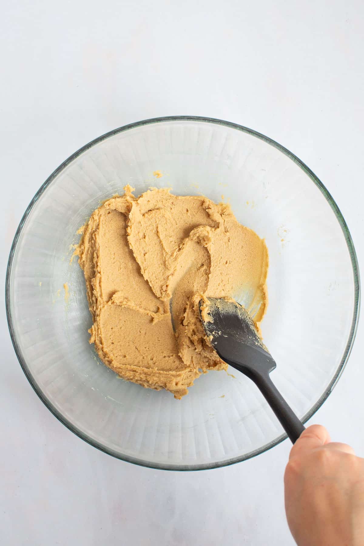 A hand using a rubber spatula to cream together butter and sugar in a bowl for small-batch chocolate chip cookies.