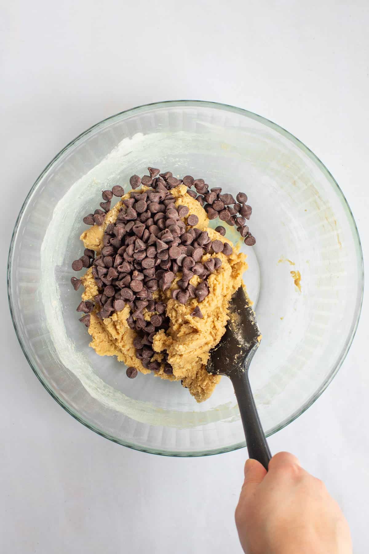 A hand using a rubber spatula to stir chocolate chips into dough in a bowl for small-batch chocolate chip cookies.