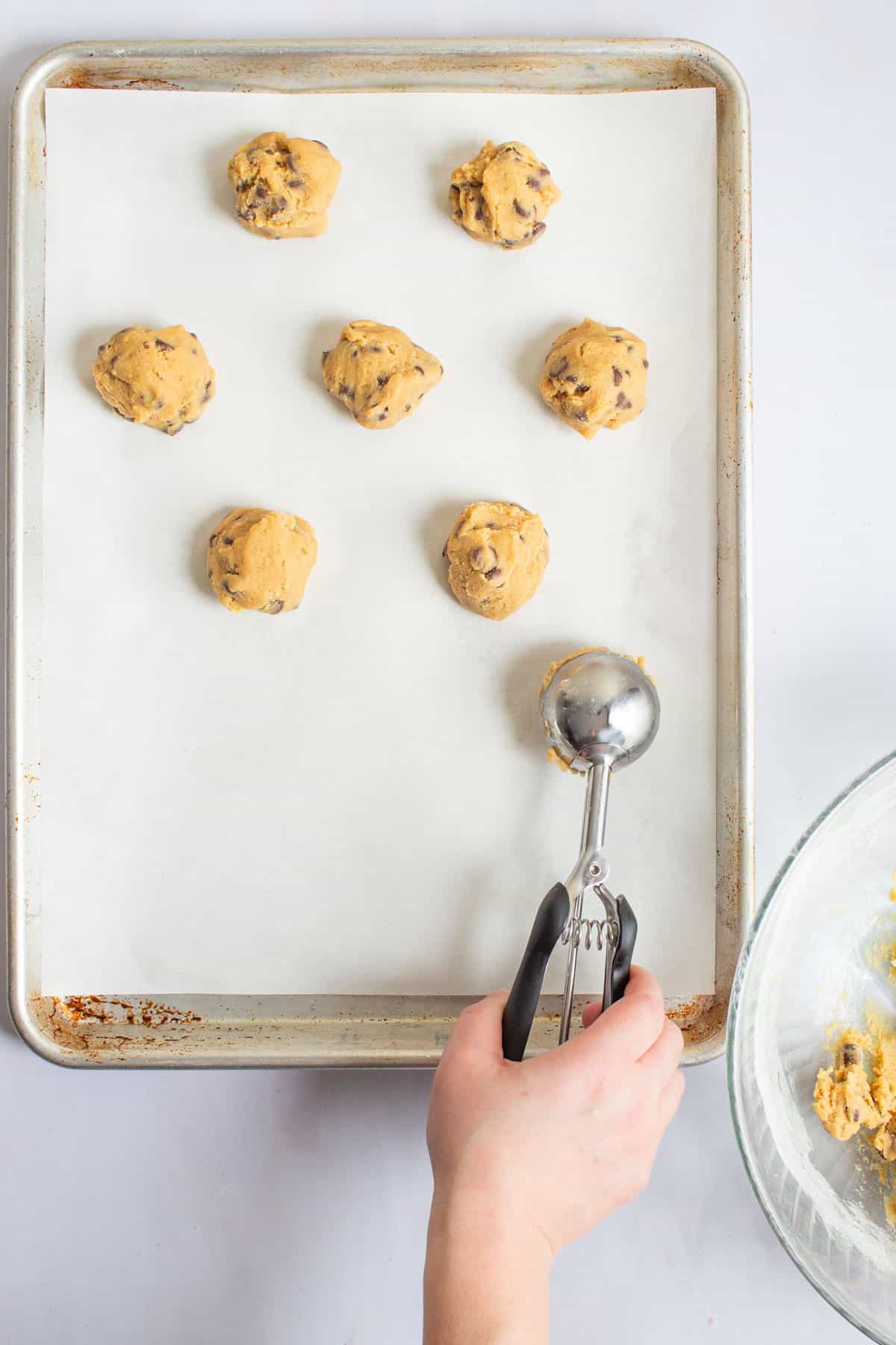 A hand using a cookie scoop to portion cookie dough onto a baking sheet for small-batch chocolate chip cookies.