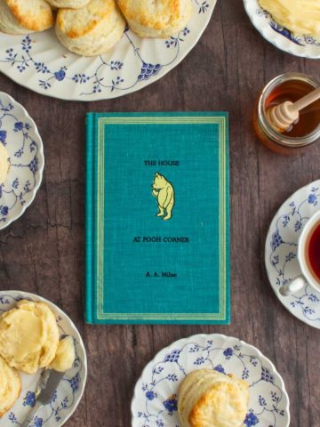 The cover of the book The House at Pooh Corner, next to plates of cream scones with homemade honey butter.