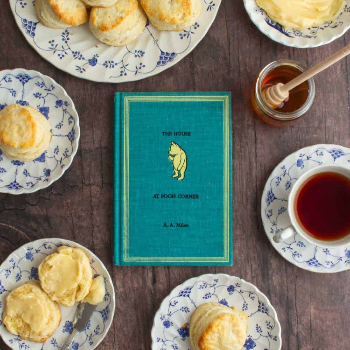 The cover of the book The House at Pooh Corner, next to plates of cream scones with homemade honey butter.