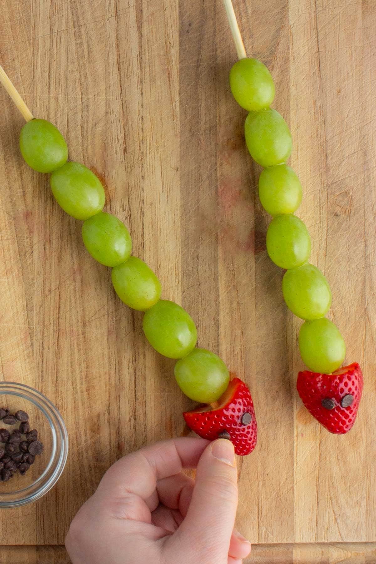 A hand pressing a mini chocolate chip into a strawberry for fruit skewers.