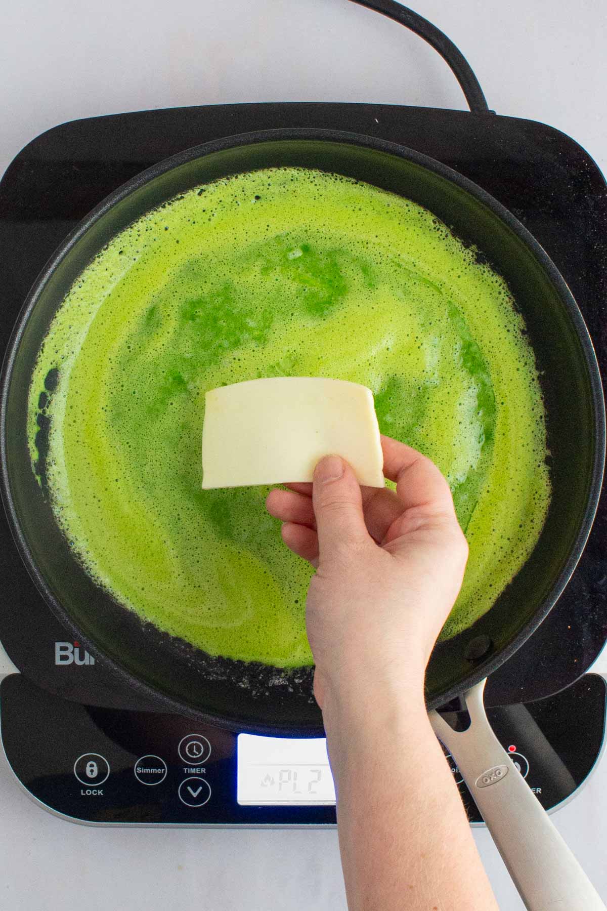 A hand placing a slice of cheese in the middle of a skillet of eggs for green eggs and ham breakfast sandwiches.