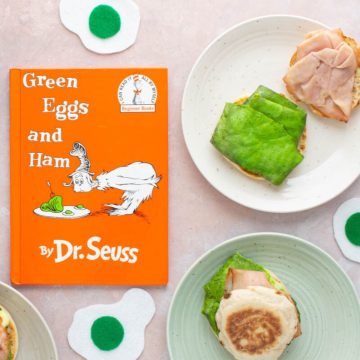 The cover of the book Green Eggs and Ham, with green eggs and ham breakfast sandwiches next to it on plates.