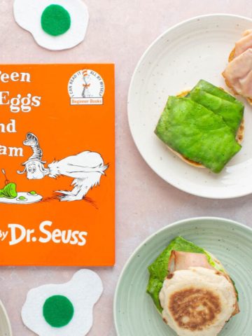 The cover of the book Green Eggs and Ham, with green eggs and ham breakfast sandwiches next to it on plates.