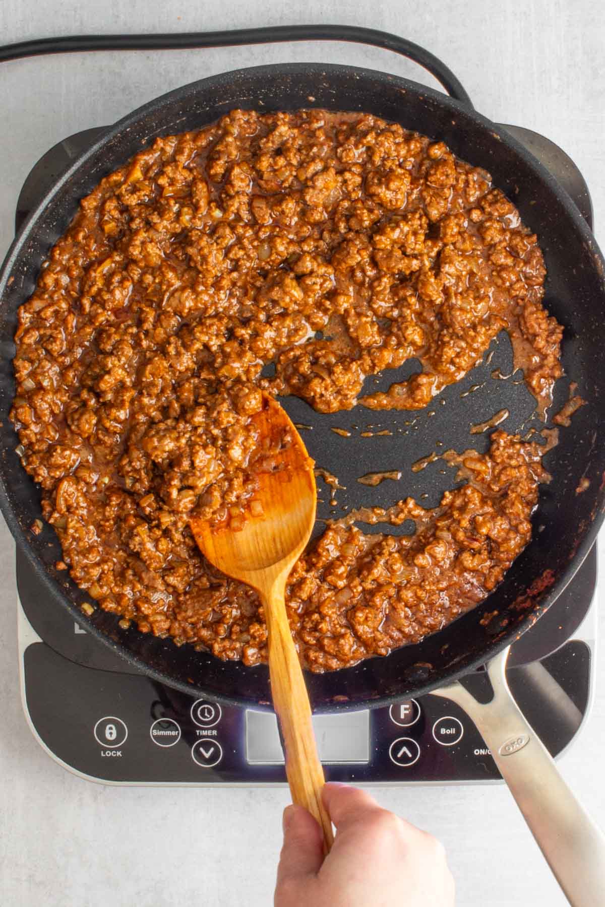 A hand using a wooden spoon to stir cooked filling for Ground Beef Tacos in a skillet.