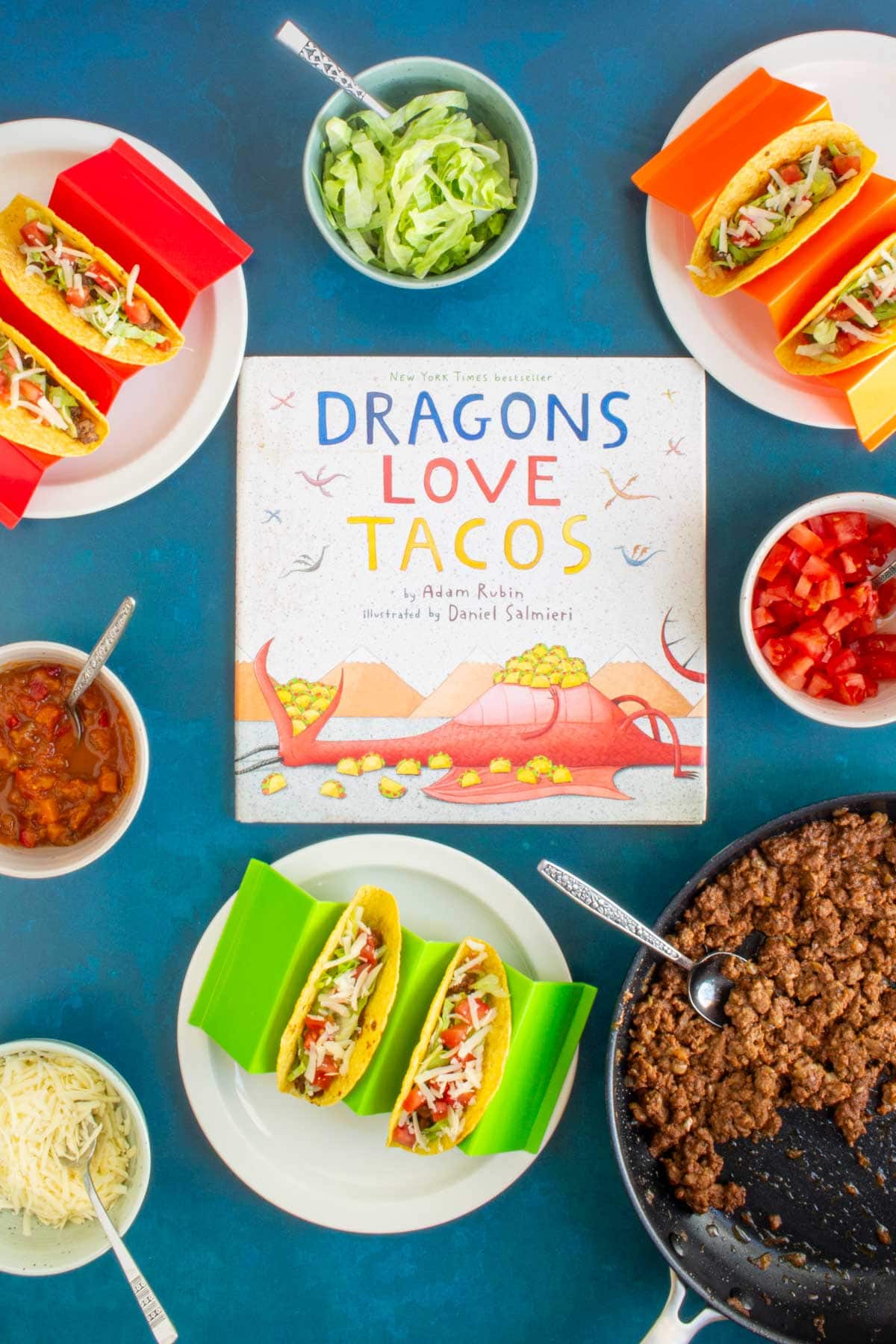 The cover of the book "Dragons Love Tacos" surrounded by a skillet of ground beef, toppings, and assembled Ground Beef Tacos.