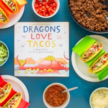 The cover of the book "Dragons Love Tacos" surrounded by a skillet of ground beef, toppings, and assembled Ground Beef Tacos.