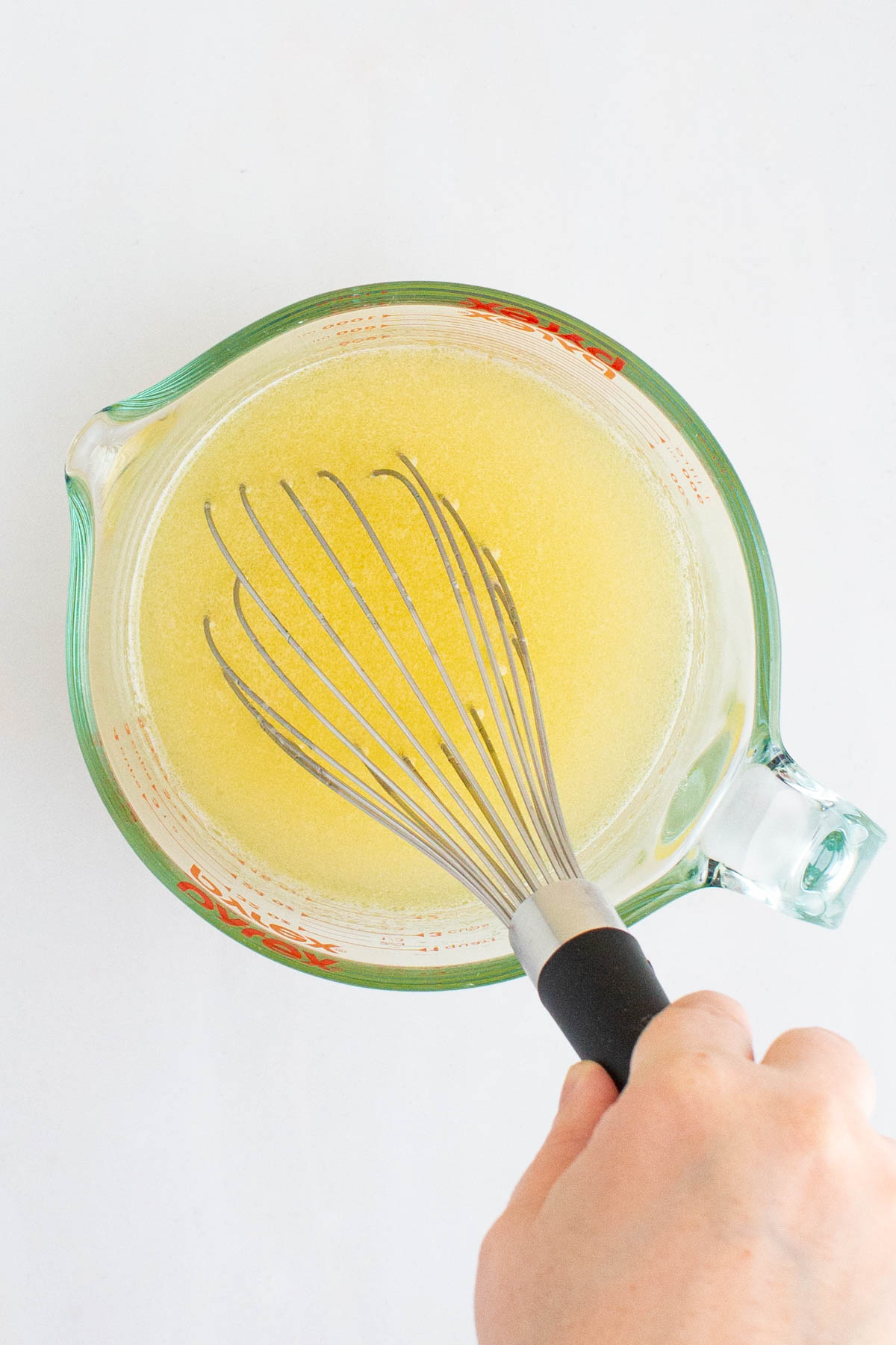 A hand whisking together water, melted butter, and honey for Easy Honey Wheat Sandwich Bread.