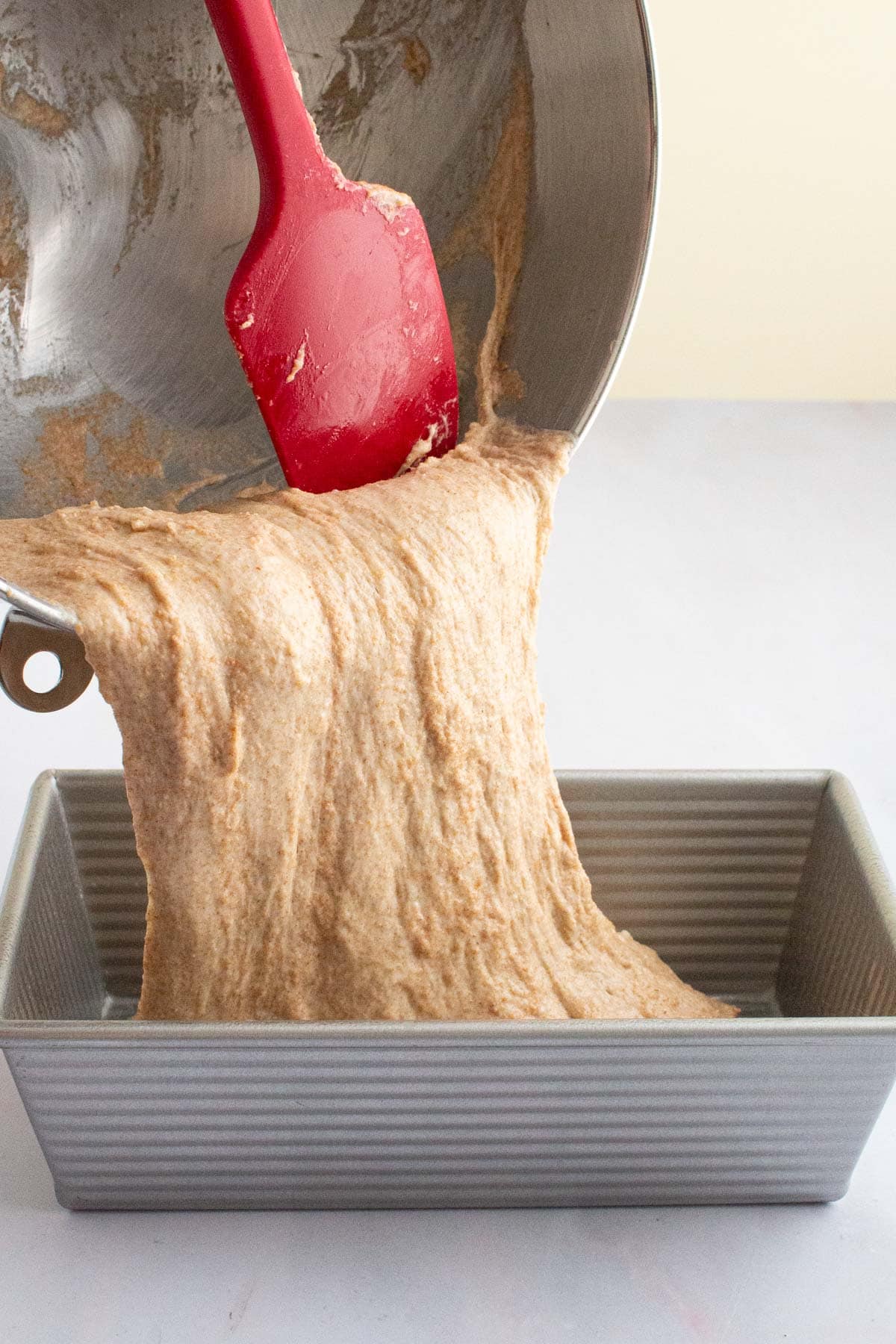 Dough for Easy Honey Wheat Sandwich Bread being scraped into a loaf pan.