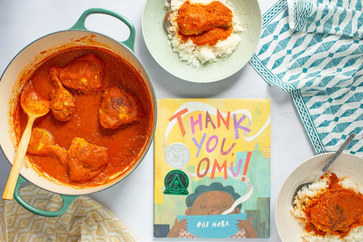 A pot and serving bowls of of Nigerian Red Stew with Chicken next to the cover of the book Thank You, Omu!