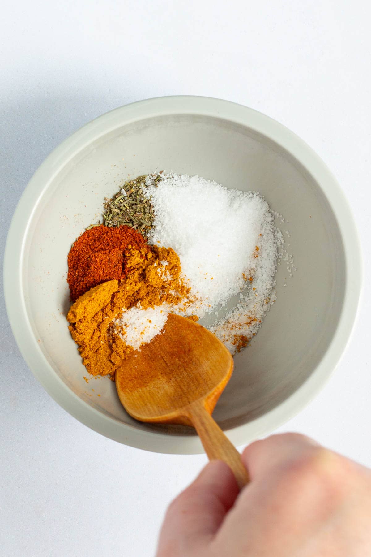 A hand using a spoon to stir together spices for Nigerian Red Stew.