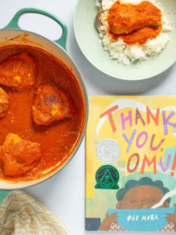 A pot and serving bowls of of Nigerian Red Stew with Chicken next to the cover of the book Thank You, Omu!