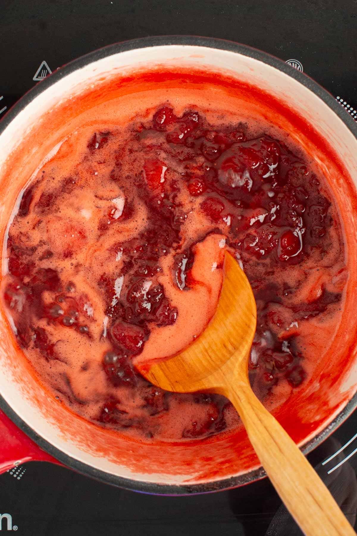 A spoon stirring together cooked strawberry rhubarb jam.