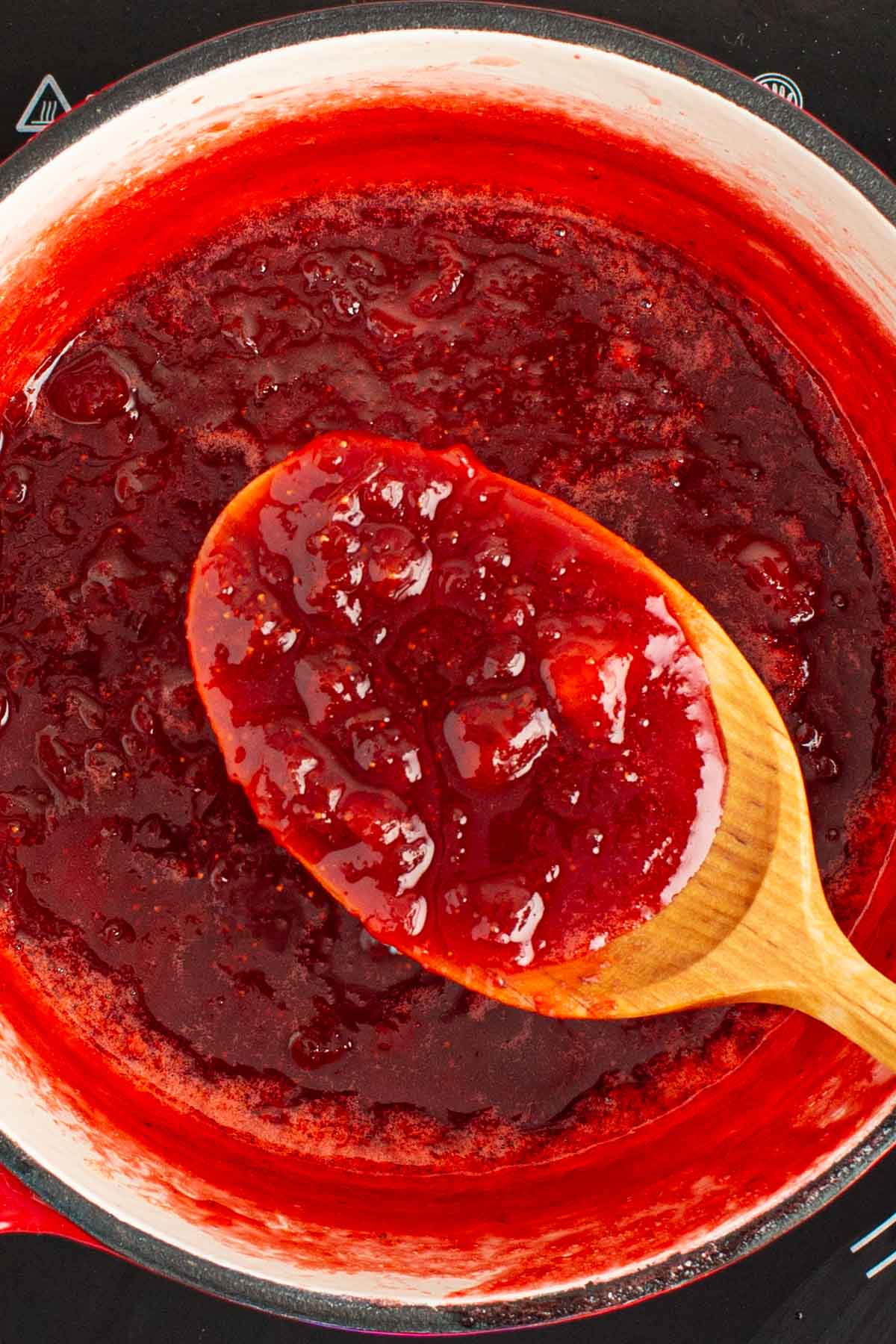 A spoon filled with cooked simple small-batch strawberry rhubarb jam.