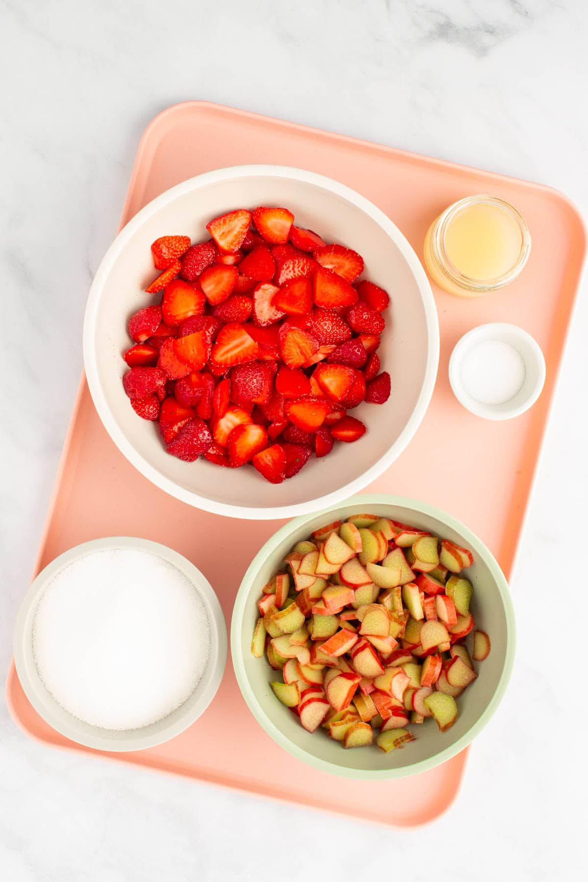 The ingredients needed to make simple small-batch strawberry rhubarb jam, measured out into bowls, set on a tray.