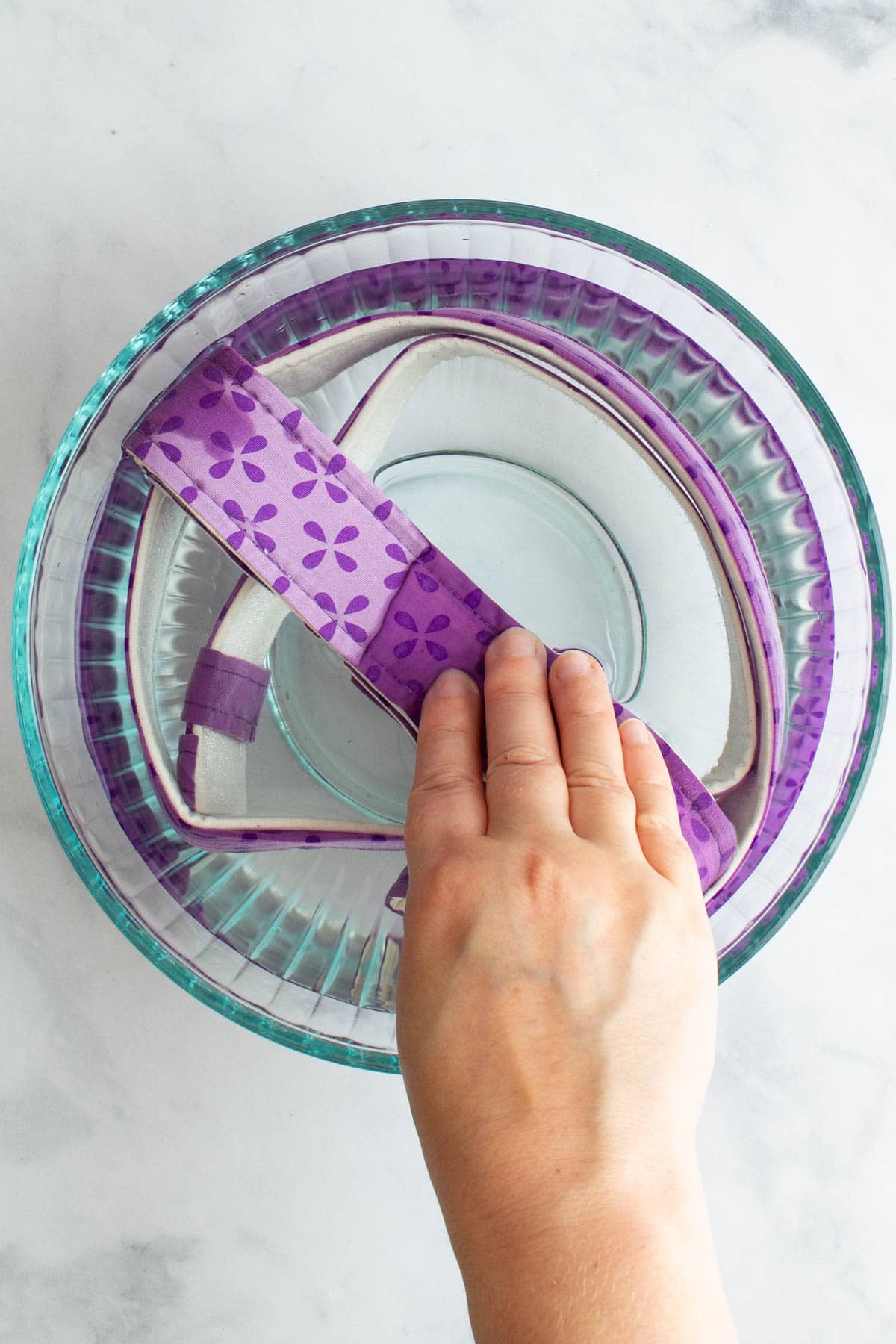 A hand pushing a cake strip down into a bowl of water.