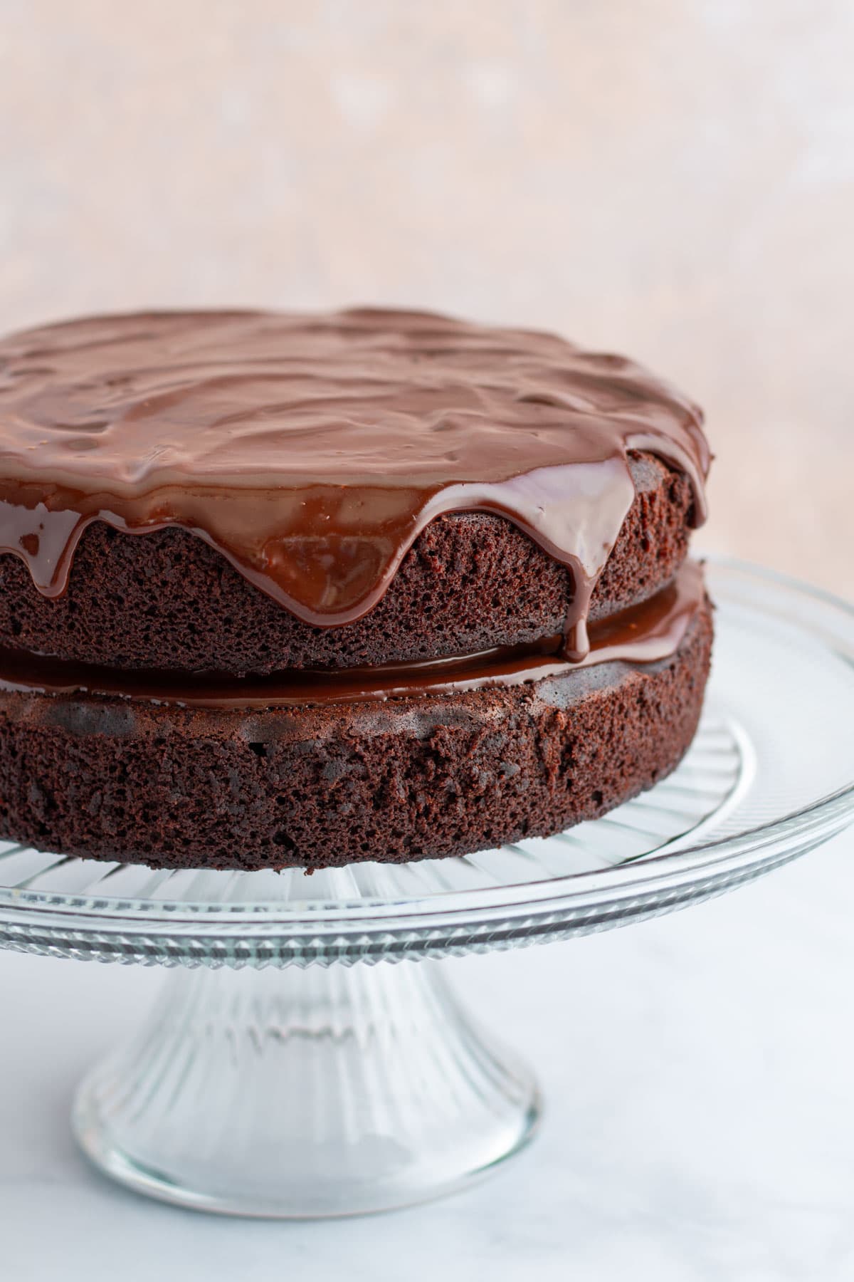 A chocolate ganache cake on a cake stand, with melted ganache dripping down the sides.