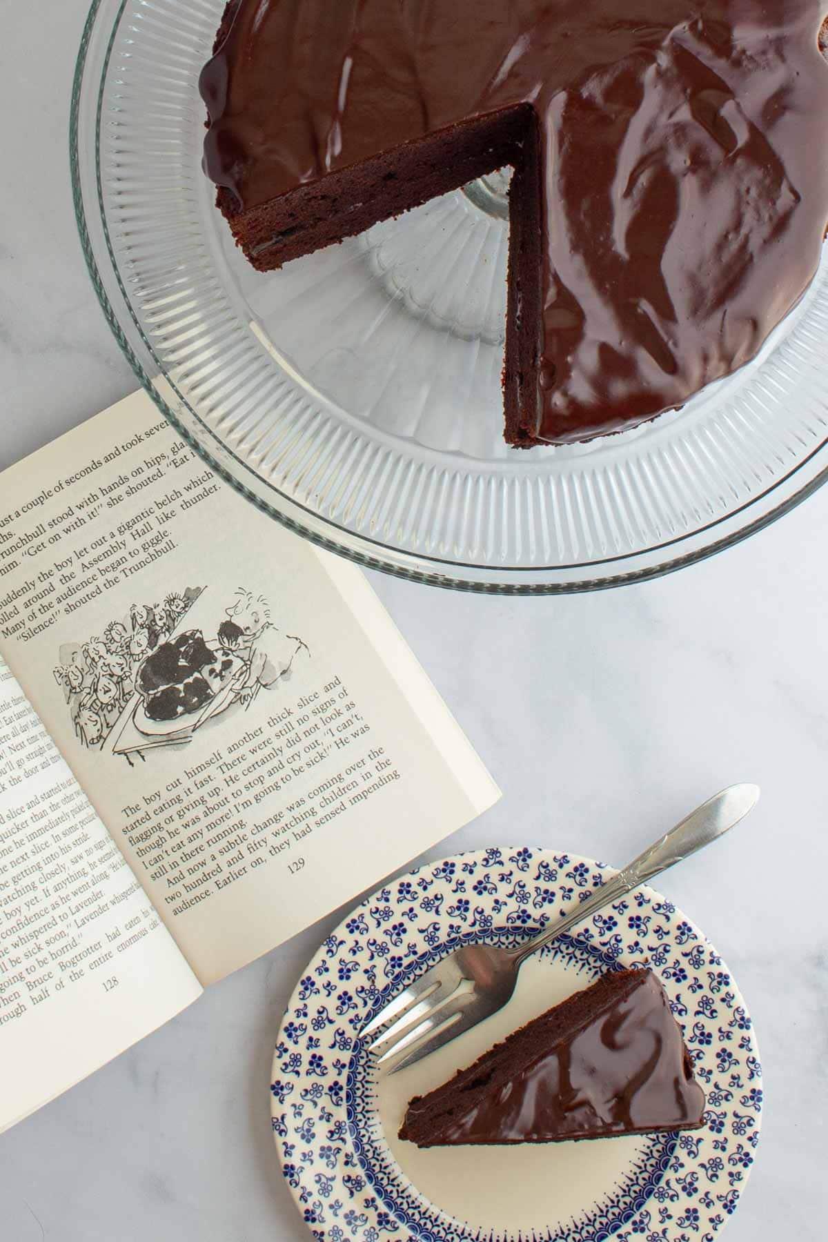 The book Matlida open to a page, with a slice of chocolate cake on a plate with a fork and the rest of the cake on a cake stand.