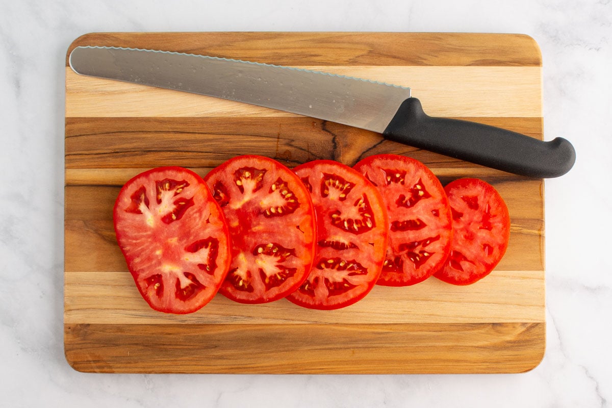 Tomato slices on a cutting board with a serrated knife.