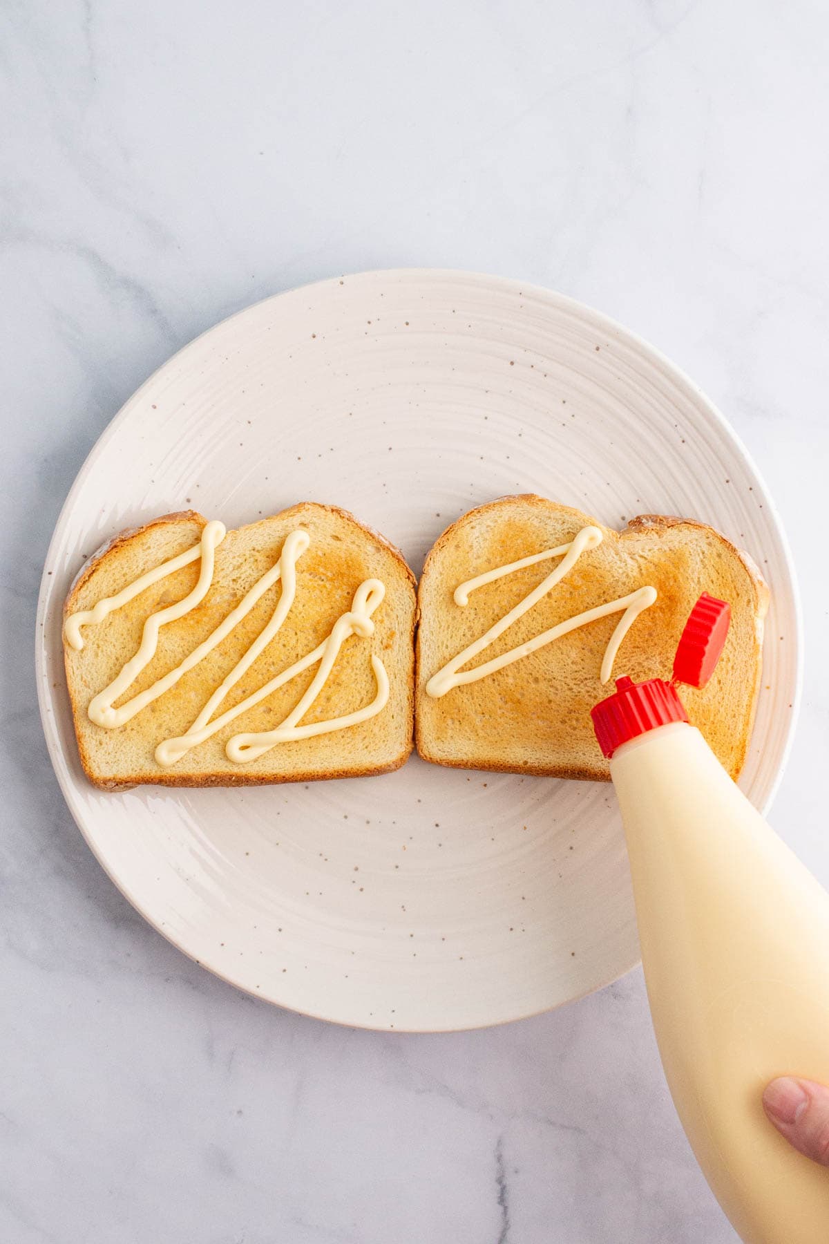 A hand squeezing Kewpie mayo onto slices of toasted bread.