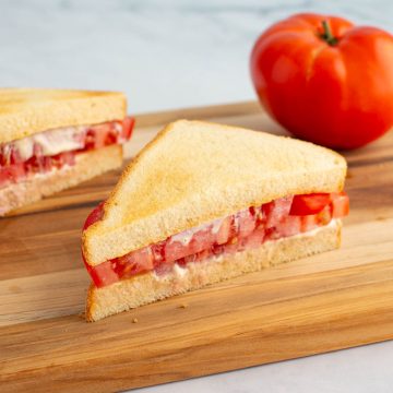 An ultimate umami tomato sandwich cut in half on a cutting board, with a tomato nearby.